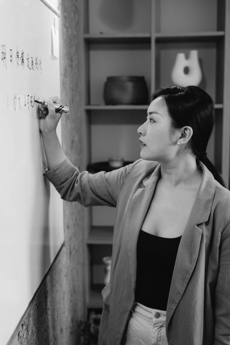 Asian businesswoman writing on a whiteboard in grayscale, captured in profile view.